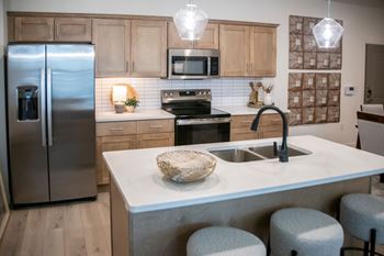 A kitchen with a refrigerator, microwave, oven, sink, and bar stools.